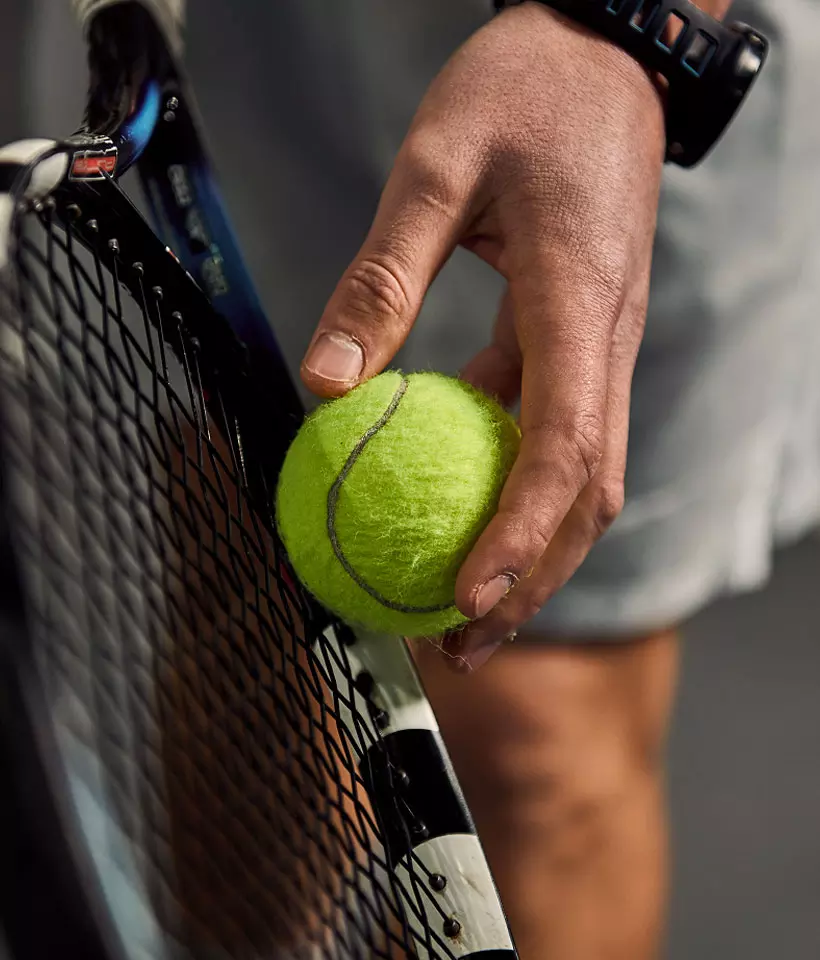 Mano sostiene una palla da tennis gialla vicino alla racchetta, pronta per colpire durante un match.